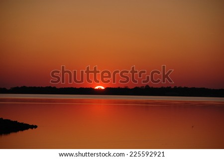The sun setting over a lake, filling the sky with a red-yellow glow.
