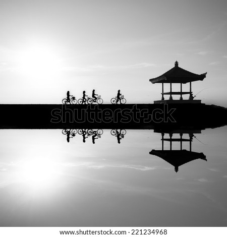 Black and white image Reflection of cyclists riding on a concrete barrier in bali indonesia Sanur beach at sunrise. This is a great place to visit when you are in Bali ..