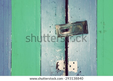 Old metal handle on colorful vertical stripes wooden door. Textured background. Pastel color. Vintage effect.