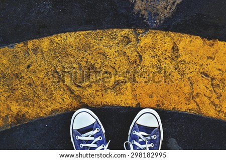 Blue Sneaker shoes standing behind yellow line. Canvas shoes on street. Top view. Vintage effect.