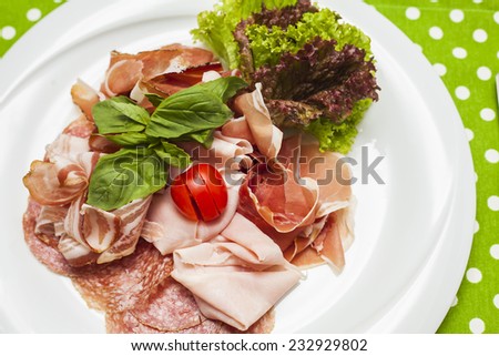 Plate with cut into pieces of meat delicacies decorated with salad leaf and cherry tomato