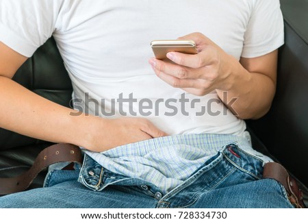 asian man or boy sitting and make a Masturbation during watching online porn or pornographic film movie in mobile phone or smartphone on sofa. focus on smartphone.