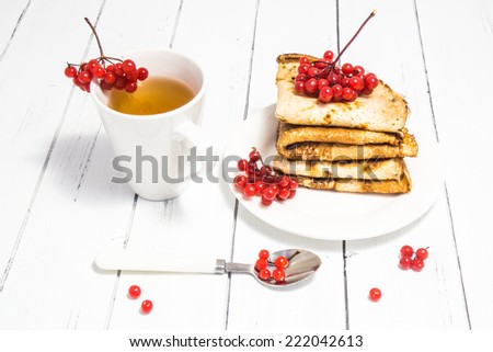 Hot tasty baked russian pancakes and red viburnum with spoon and cup of tea on a white wooden background. Holiday table for Shrovetide. Delicious breakfast