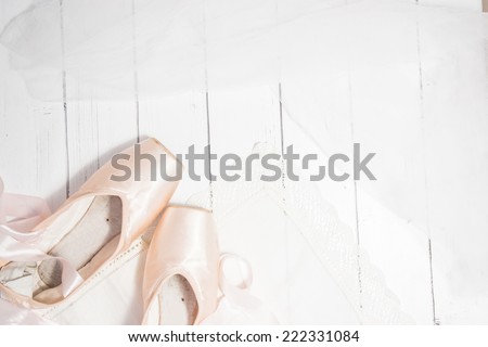 Pair of two satin russian pink ballet pointes with long ribbons lying on a white wooden background. Shabby chic vintage style