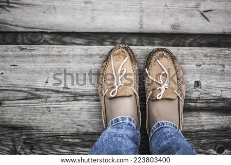 two legs wearing orange chamois moccasins with ties and denim jeans on wooden background near the sea