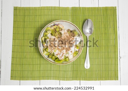 fresh fruit salad in a plate on a green bamboo mat and white wooden table with metal spoon