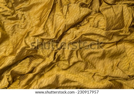 Thin shiny golden cloth background with shiny uneven surface with drapery and wrinkles