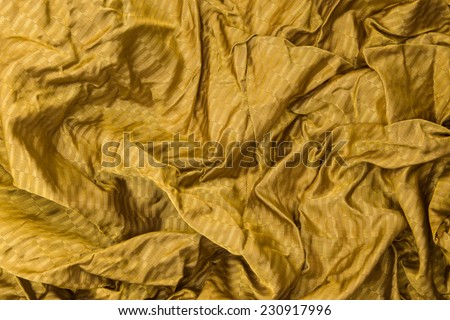 Thin shiny golden cloth background with shiny uneven surface with drapery and wrinkles