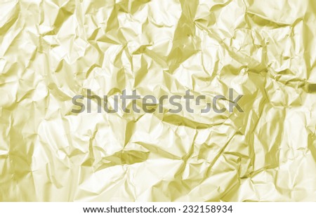 Thin sheet of silver leaf background with shiny crumpled uneven surface yellow gold color