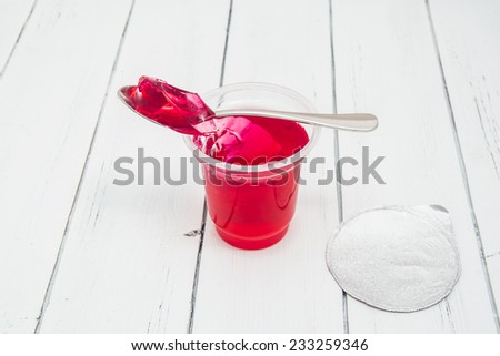 Plastic container for dairy foods with red clear jelly pudding with foil lid and spoon. Isolated on a white.