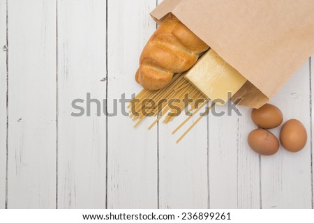 Food from supermarket in a paper craft bag on a white wooden background.