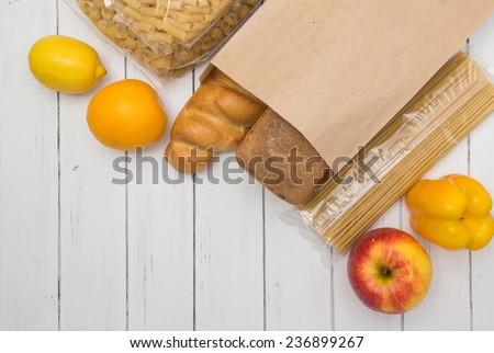 Food from supermarket in a paper craft bag on a white wooden background. Fruits, vegetables, bread, pasta