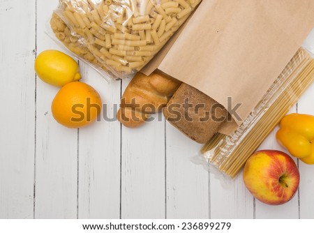 Food from supermarket in a paper craft bag on a white wooden background. Fruits, vegetables, bread, pasta