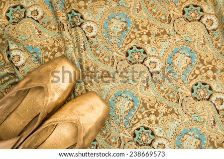 Colored golden old ballet shoes pointe on a oriental Indian cloth background with golden floral pattern