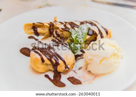 Appetizing apple strudel pie with ice-cream ball, mint leaf and chocolate drops on a white plate in a restaurant