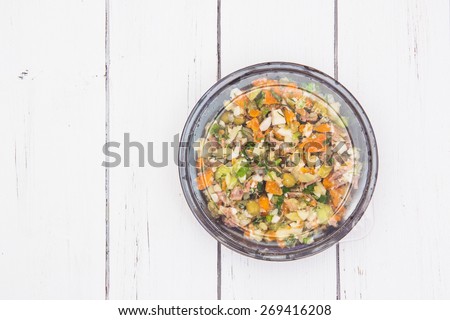 Olivier traditional salad in a black plastic container isolated on a white wooden background.