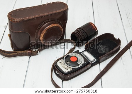 Retro photo camera in a leather case with a photometer and a film on a white wooden background