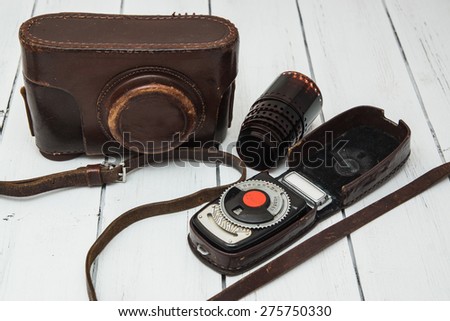 Retro photo camera in a leather case with a photometer and a film on a white wooden background