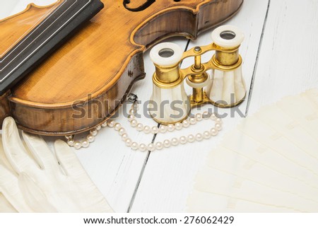 Vintage backgrop with violin, white leather gloves, fan, pearl beads and binoculars on a white wooden background