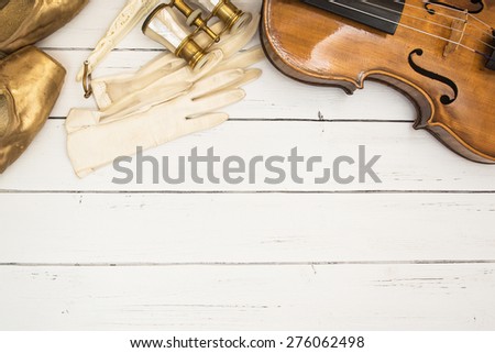Vintage backgrop with violin, white leather gloves, golden ballet pointes and binoculars on a white wooden background