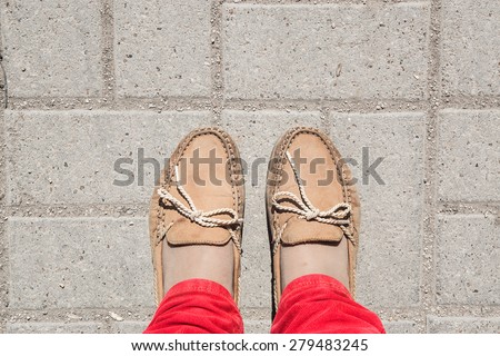 two legs wearing orange chamois moccasins with ties and red corduroy jeans on brick background in a sunny day