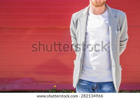 Man wearing jeans, white T-shirt and grey jacket standing near a red wall