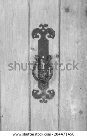 Black and white photo - vintage forged iron door lock on a wooden door