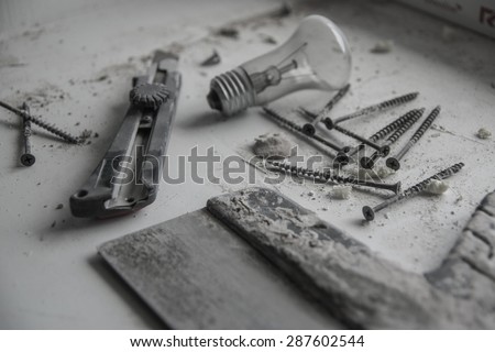 Sad house repair still life with spatula, screw, bulb,and knife on a dirty surface