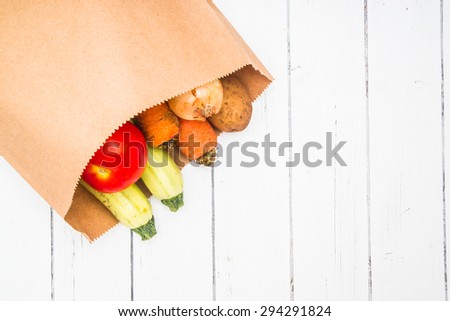 Vegetables in a craft paper bag from market on a white wooden table