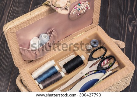 Braided sewing box with tools and buttons on a dark wooden table