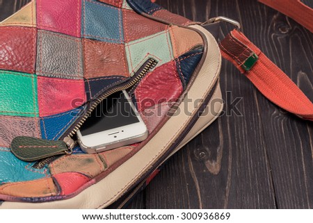 Stylish bright leather bag of square colorful patches. Close-up photo with pocket and zipper and a phone inside
