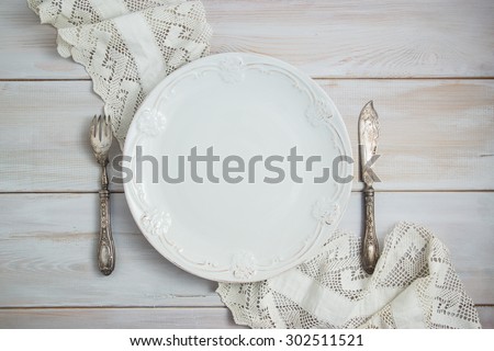 Served table with an antique table, silver folk and knife with lace cotton napkin on a white wooden table