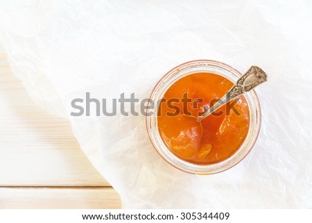Tasty orange apricot jam in a glass jar  with a spoon on white wooden background