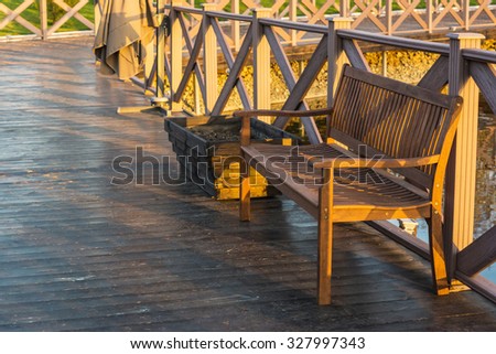 Equipped bank of pond for walk rest and fishing. Wooden fence with bench on a wooden floor on a sunset