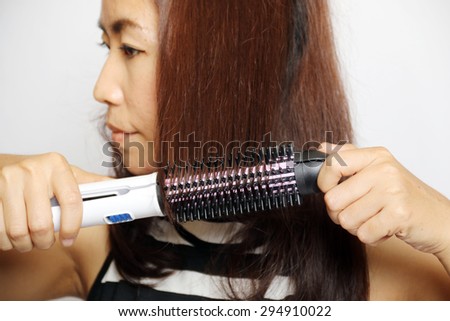 A woman using a curling iron on a white background.