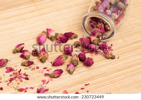 Dried roses, wooden scoop of rose tea on bamboo mat