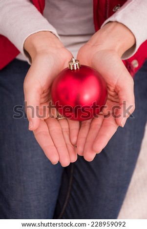 A woman\'s hand cup a red Christmas ornament as if cherishing the spirit of the season.