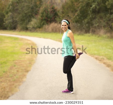 An athletic woman stretches on a running path outside.