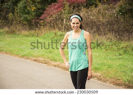 An athletic woman stands on a running path. She has a big beautiful smile.