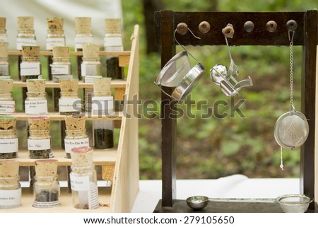 Tea in glass tubes in a display stand and tea strainers hanging from wooden pegs on display for sale at a fair.