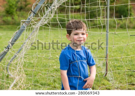 A little boy pressing his face into a goal net, outside on a spring day. Horizontal.