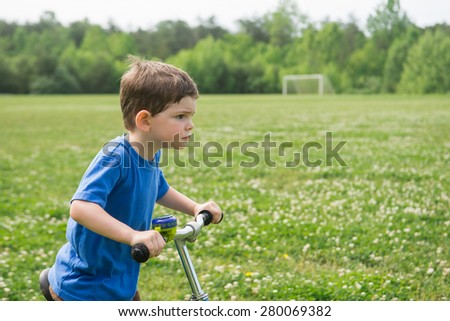 A boy on a bike in the grass wearing a blue shirt, with a determined look on his face. Spring setting, horizontal. Room for copy.