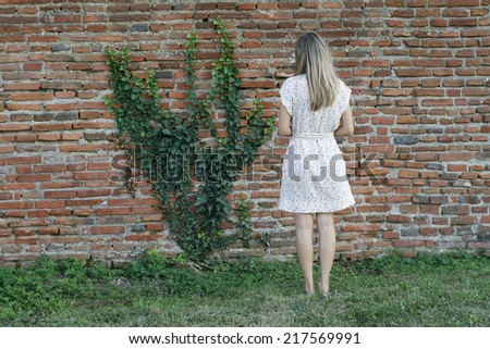 Young woman in front of brick wall with green plant growing