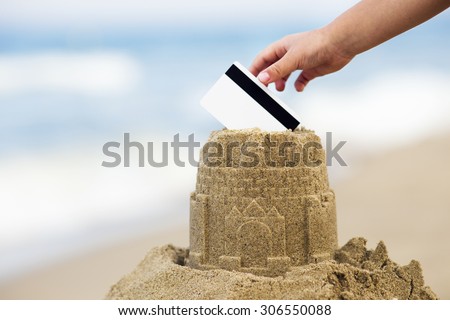 Sand castle tower with hand and credit card. Payment for holidays vacation concept
