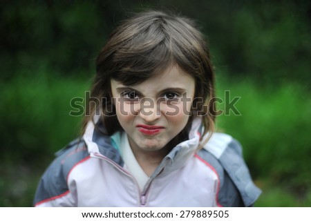 Angry child. Young girl making funny grimace face on a green background..
