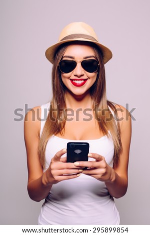 Funky beauty with mobile phone. Portrait of beautiful young woman in glasses and funky hat holding mobile phone