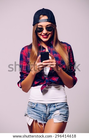Funky beauty with mobile phone. Portrait of beautiful young woman in glasses and funky hat holding mobile phone