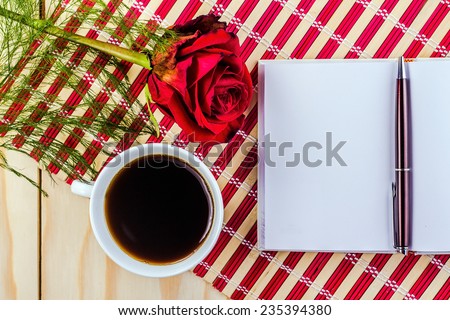 open notepad, cup of coffee and rose on red striped napkin