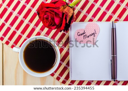 open notepad, cup of coffee and rose on striped napkin