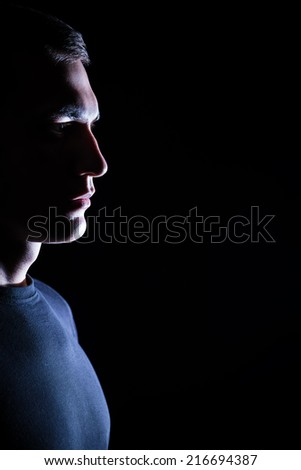 Serious young man standing in profile in dark studio